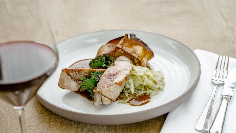 A plate of pheasant breast, kale and cabbage, with a glass of red wine next to it.