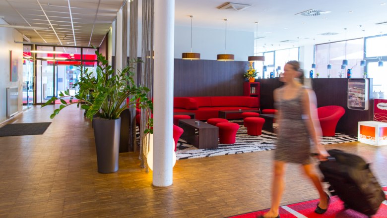 Hotel-Lobby mit rotem Sofa und Frau mit Koffer.