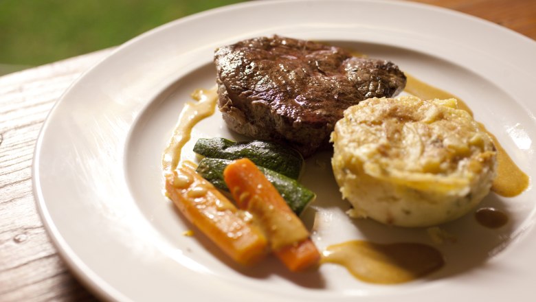Ein Teller mit einem St&uuml;ck Fleisch, Gem&uuml;se und einer Kartoffelbeilage.