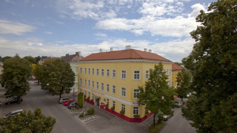 Außenansicht eines gelben Hotels mit rotem Dach, umgeben von Bäumen und Straßen.