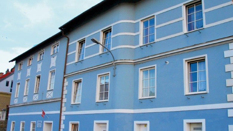Modr&aacute; fas&aacute;da v&iacute;cepodlažn&iacute; budovy s b&iacute;l&yacute;mi r&aacute;my oken a dveř&iacute;.