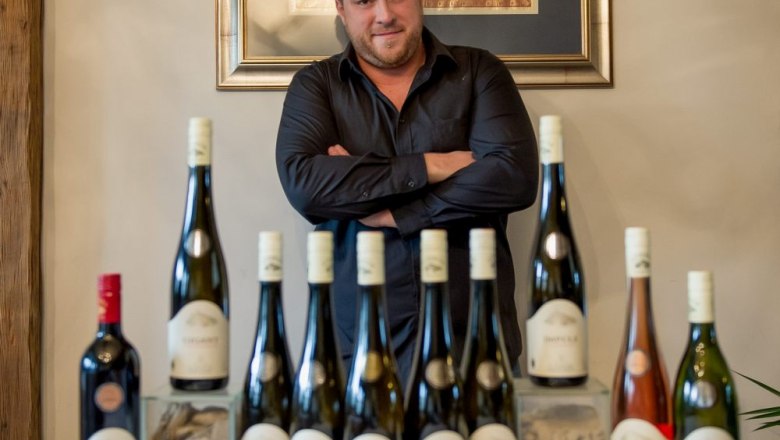Man standing behind a row of wine bottles on a table.