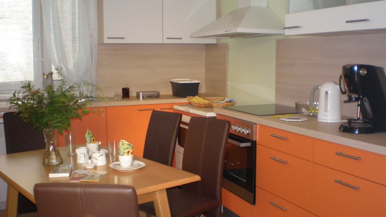 Modern&iacute; kuchyň s oranžov&yacute;mi skř&iacute;ňkami, j&iacute;deln&iacute;m stolem se židlemi, k&aacute;vovarem a rychlovarnou konvic&iacute;.