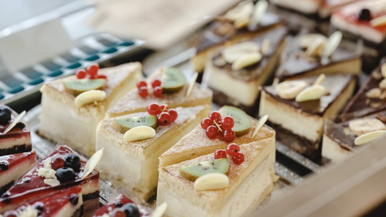 Verschiedene Kuchenstücke in einer Vitrine, dekoriert mit Früchten und Schokolade.