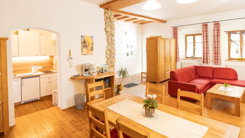 Gem&uuml;tliches Wohnzimmer mit Holzm&ouml;beln, rotem Sofa und offener K&uuml;che.
