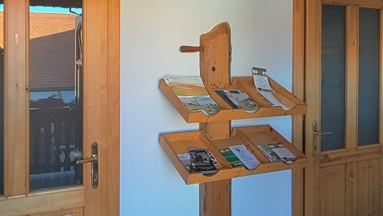 Dřevěn&aacute; police s brožurami na b&iacute;l&eacute; stěně mezi dvěma dřevěn&yacute;mi dveřmi.