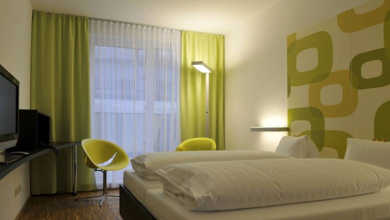Modernes Hotelzimmer mit Doppelbett, gr&uuml;n-gelben Vorh&auml;ngen und Wanddekor.