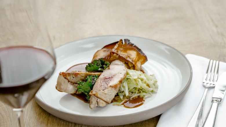 Ein Teller mit Fasanbrust, Gr&uuml;nkohl und Kraut, daneben ein Glas Rotwein.