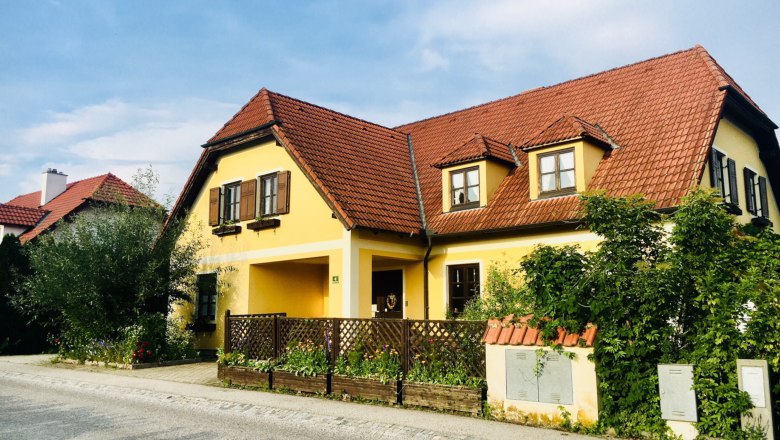 Gelbes Landhaus mit rotem Ziegeldach und Garten.