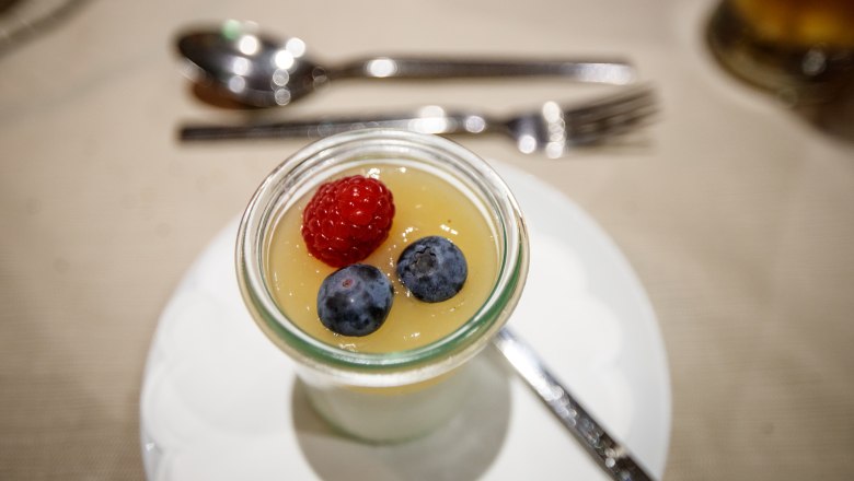 Dezert ve sklenici s malinami a borůvkami na ubrusu.