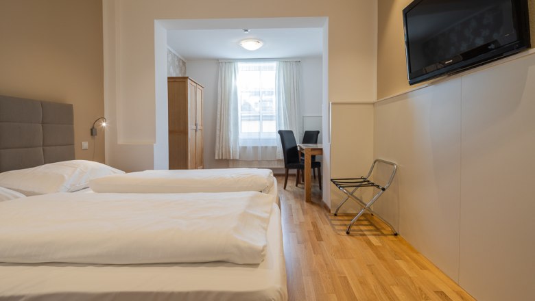 Hotelzimmer mit zwei Betten, Fernseher, Tisch und Stühlen.