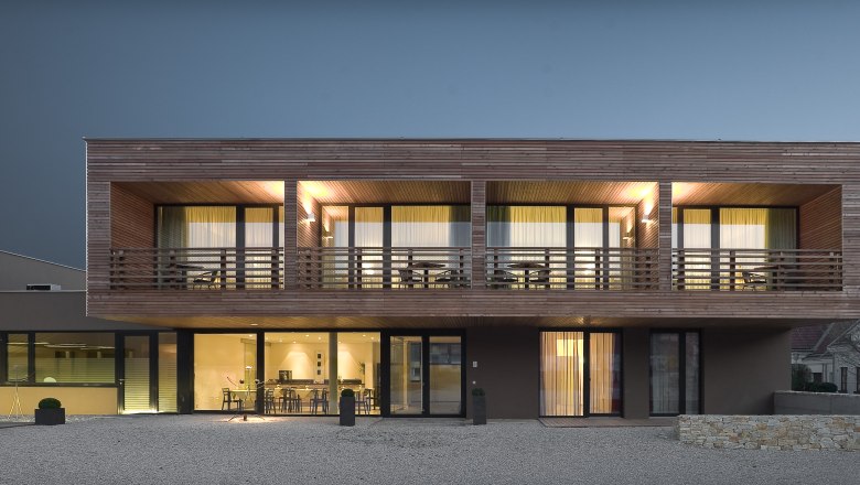 Modernes zweistöckiges Haus mit Holzverkleidung und großen Fenstern bei Nachtbeleuchtung.