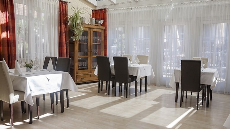Innenansicht eines hellen Restaurants mit gedeckten Tischen und Stühlen.