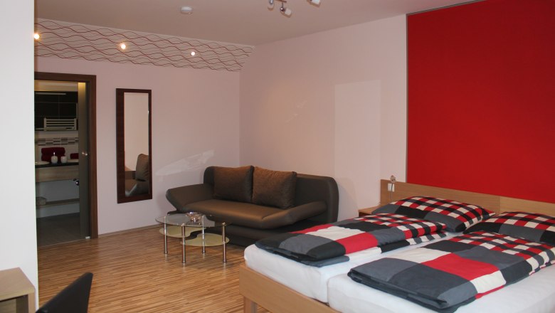 Modern furnished guest room with double bed, sofa and small table.