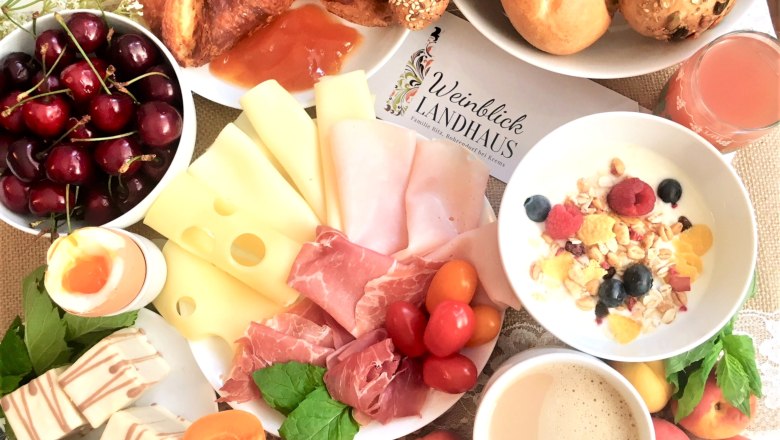 Ein reichhaltiges Frühstück mit Käse, Schinken, Croissants, Obst, Müsli, Ei und Kaffee auf einem Tisch.