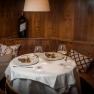 Cozy dining room with set table, two plates with food and wine glasses, wooden wall and cushions.