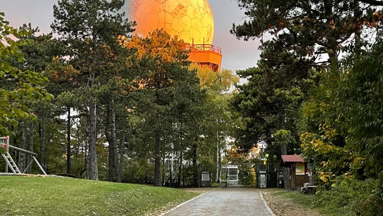 Cesta vede lesem k velk&eacute; kulovit&eacute; stavbě, kterou osvětluje slunce.