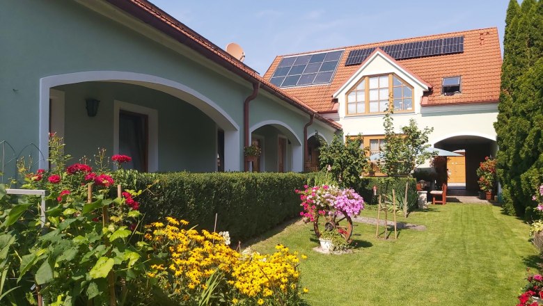 Udržovan&aacute; zahrada s barevn&yacute;mi květinami a dům se sol&aacute;rn&iacute;mi panely na stře&scaron;e.