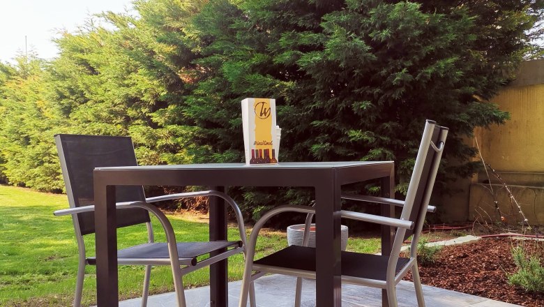 Terrasse mit Tisch, zwei St&uuml;hlen und B&auml;umen im Hintergrund.