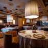 Elegantn&iacute; restaurace s kulat&yacute;mi stoly, b&iacute;l&yacute;mi ubrusy a velk&yacute;mi z&aacute;věsn&yacute;mi lampami.