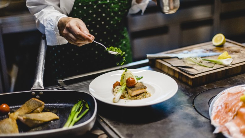 Koch dekoriert ein Gericht mit Kr&auml;utern in einer K&uuml;che.