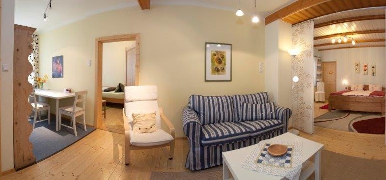 Panorama eines gem&uuml;tlichen Wohnzimmers mit Sofa, Esstisch und Schlafzimmer im Hintergrund.