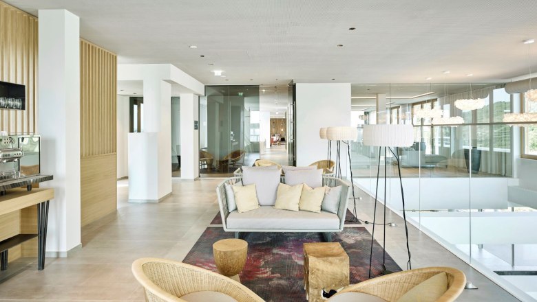 Moderner Aufenthaltsbereich im Hotel-Spa mit heller Einrichtung, Sofas, Stehlampen und einer Kaffeemaschine.