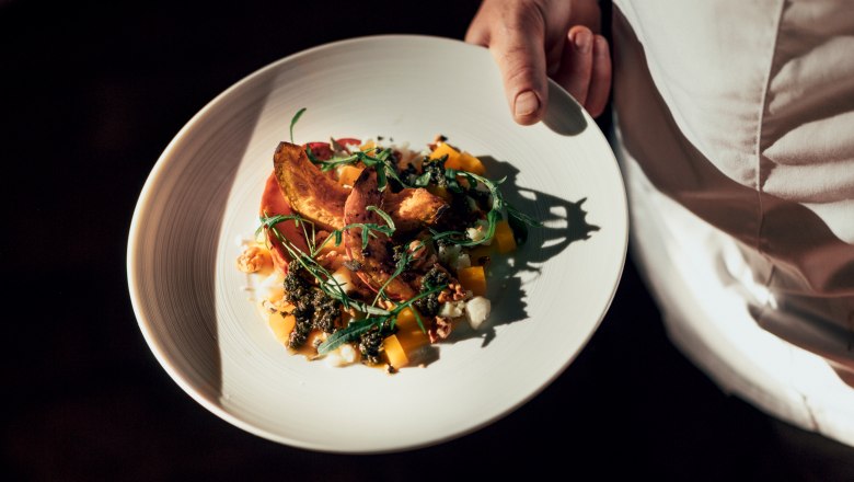 Tal&iacute;ř s pečlivě naaranžovan&yacute;m pokrmem, kter&yacute; drž&iacute; osoba v b&iacute;l&eacute;m oděvu.