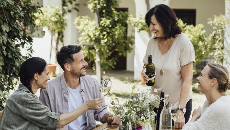 Vier Personen sitzen an einem Tisch im Freien und genießen Wein und Brot.
