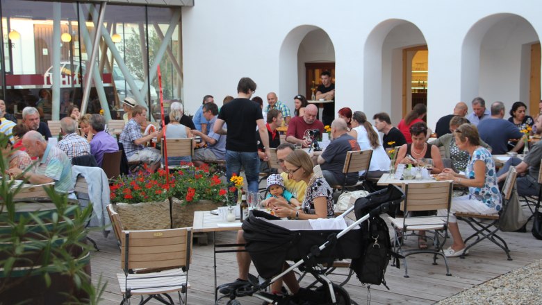 Menschen sitzen in einem Innenhof an Tischen und essen.