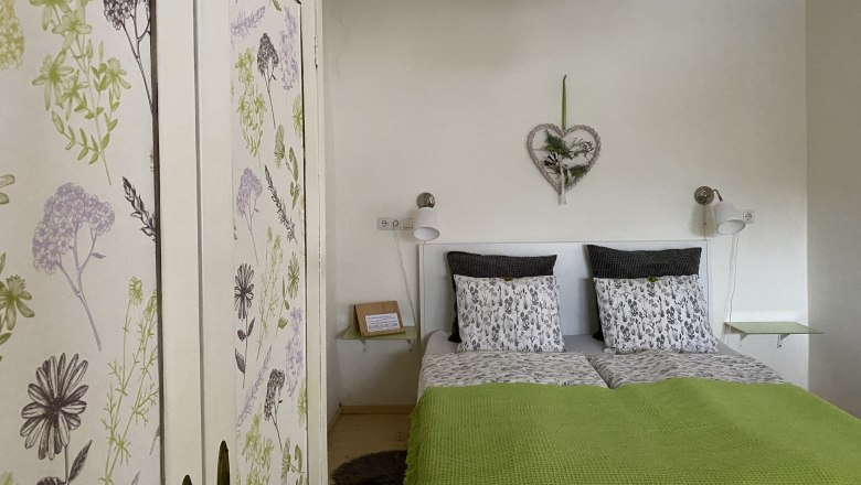 Gemütliches Doppelzimmer mit floralem Kleiderschrank und grüner Bettdecke.