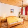 Gem&uuml;tliches Schlafzimmer mit Holzm&ouml;beln, gelber Bettw&auml;sche und roten Vorh&auml;ngen.