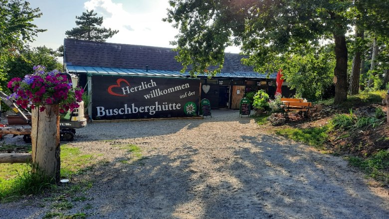 Eingangsbereich der Buschberghütte mit Willkommensschild und Blumen.