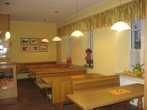 Innenansicht eines gem&uuml;tlichen Caf&eacute;s mit Holztischen und B&auml;nken, dekoriert mit Bildern und Pflanzen.