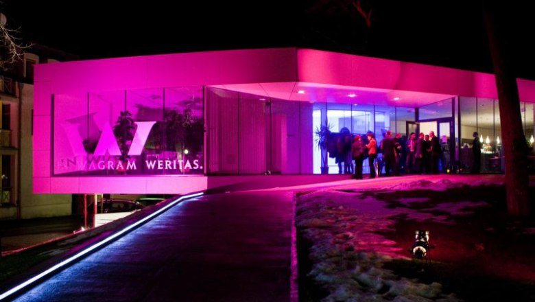 Moderne Vinothek bei Nacht mit pinker Beleuchtung und Menschen am Eingang.