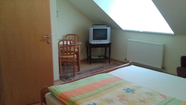 Ein einfach eingerichtetes Zimmer mit Bett, Fernseher und Tisch unter einer Dachschräge.