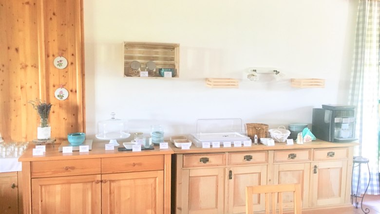 Frühstücksbuffet auf einem Holzbuffet mit Geschirr, Gläsern und einer Kaffeemaschine.