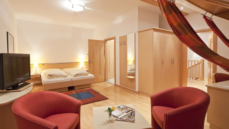 Gem&uuml;tliches G&auml;stezimmer mit Doppelbett, TV, roten Sesseln und H&auml;ngematte.