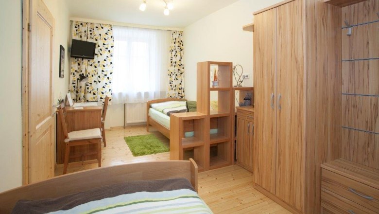 A bright bedroom with wooden furniture, two beds, a desk and a small TV on the wall.