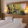 A cozy guest room with two single beds, a large picture of grapes above the bed and two wall lamps.