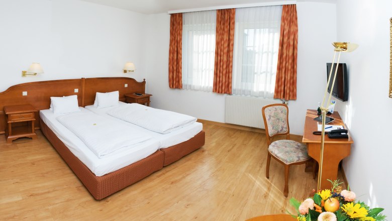 Ein gemütliches Doppelzimmer mit zwei Betten, Holzmöbeln und einem Schreibtisch mit Stuhl.