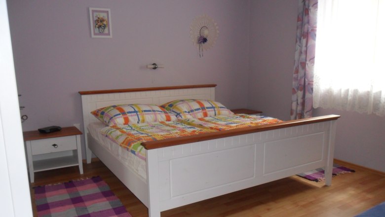A bedroom with a white bed, colorful comforters, a bedside table and a window with curtains.