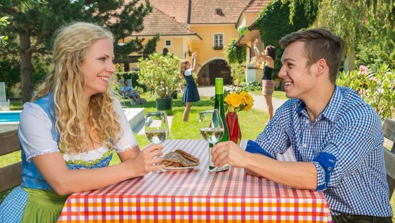 Zwei Personen sitzen an einem Tisch im Freien und trinken Wein.