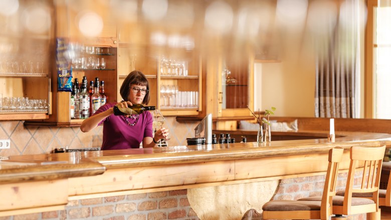 Eine Frau steht hinter einer Bar in einem rustikalen Restaurant und schenkt Wein ein.