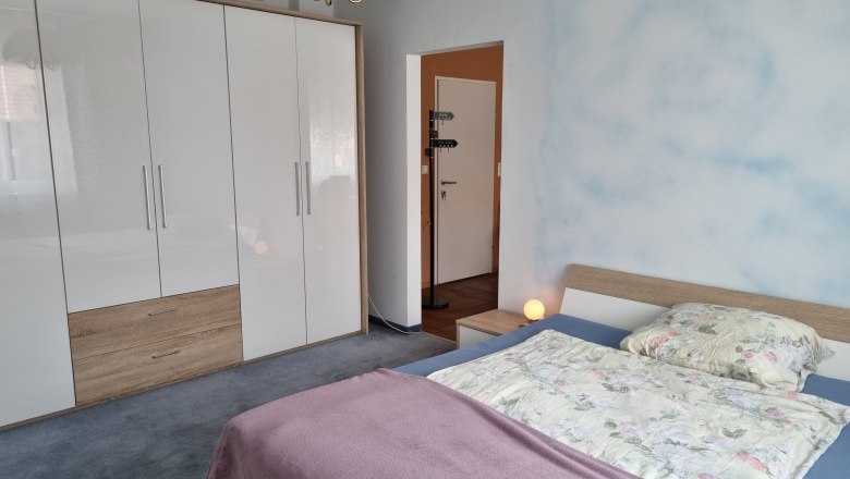 Ložnice s manželskou postel&iacute;, velkou b&iacute;lou skř&iacute;n&iacute; a nočn&iacute; lampou.