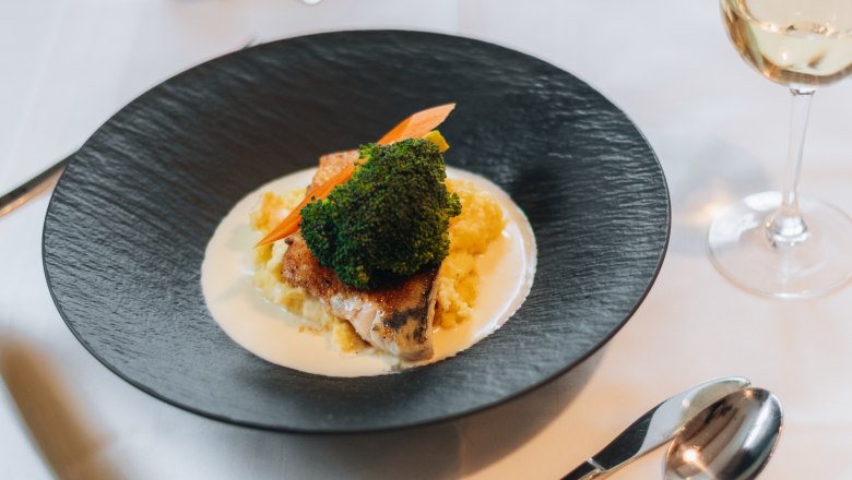 Elegantně prezentovan&yacute; pokrm na čern&eacute;m tal&iacute;ři se zeleninou a om&aacute;čkou, doplněn&yacute; sklenkou b&iacute;l&eacute;ho v&iacute;na na prostřen&eacute;m stole.