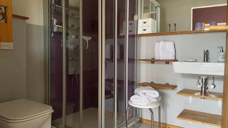 Modern&iacute; koupelna se sprchou, umyvadlem, ručn&iacute;ky a poličkami.