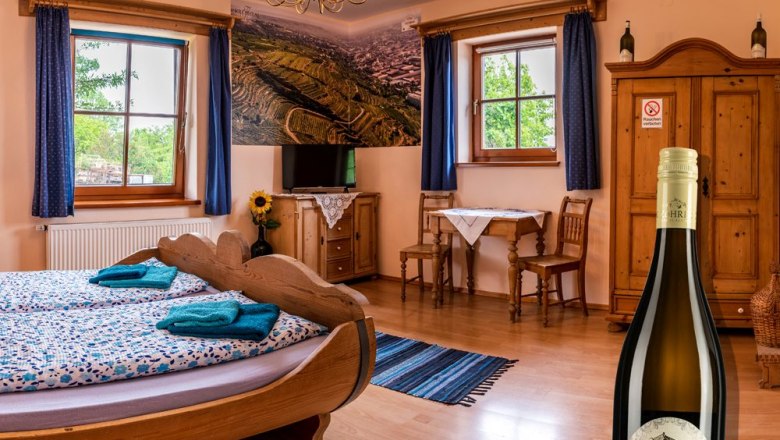 Cozy room with wooden furniture, a barrel bed and a bottle of wine in the foreground.