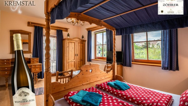 A cozy room with a four-poster bed, wooden furniture and a view of the vineyards. A bottle of wine is pictured in the foreground.