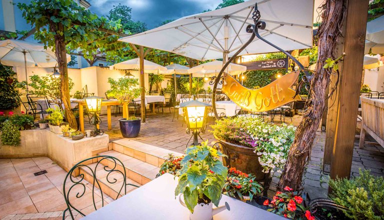 Gastgarten am Abend mit Beleuchtung und vielen Sitzmöglichkeiten, Pflanzen und Schirmen.